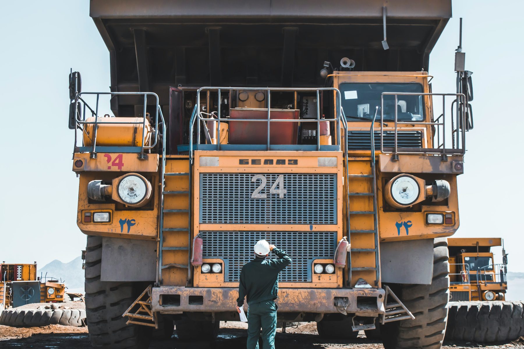 A single worker in a hard hat standing in front of a very large mining haul truck