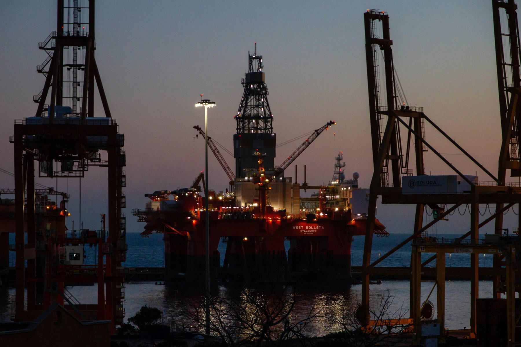 Port cranes and a drilling rig lit up at dusk