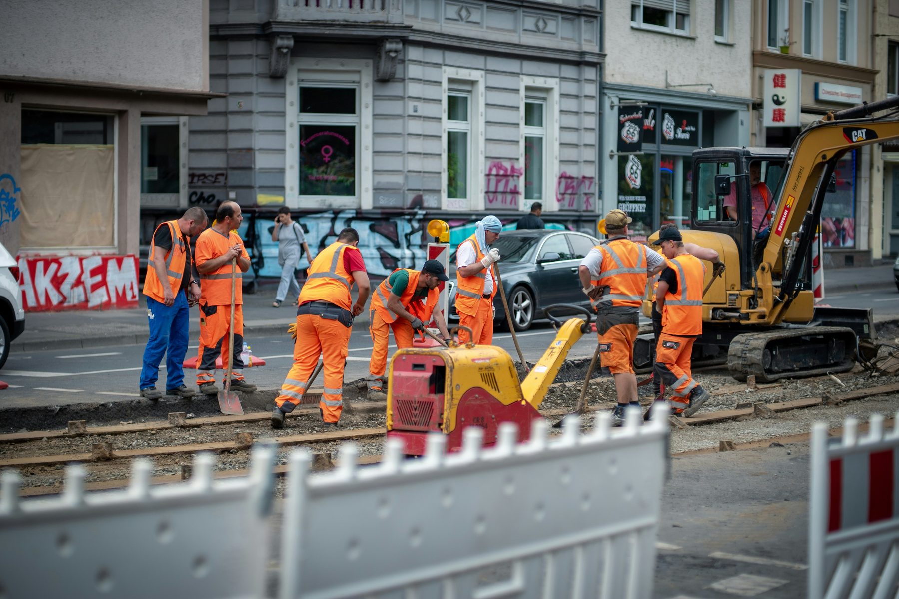 A road crew in orange high-visibility clothing working on a tram line in a city street behind barriers